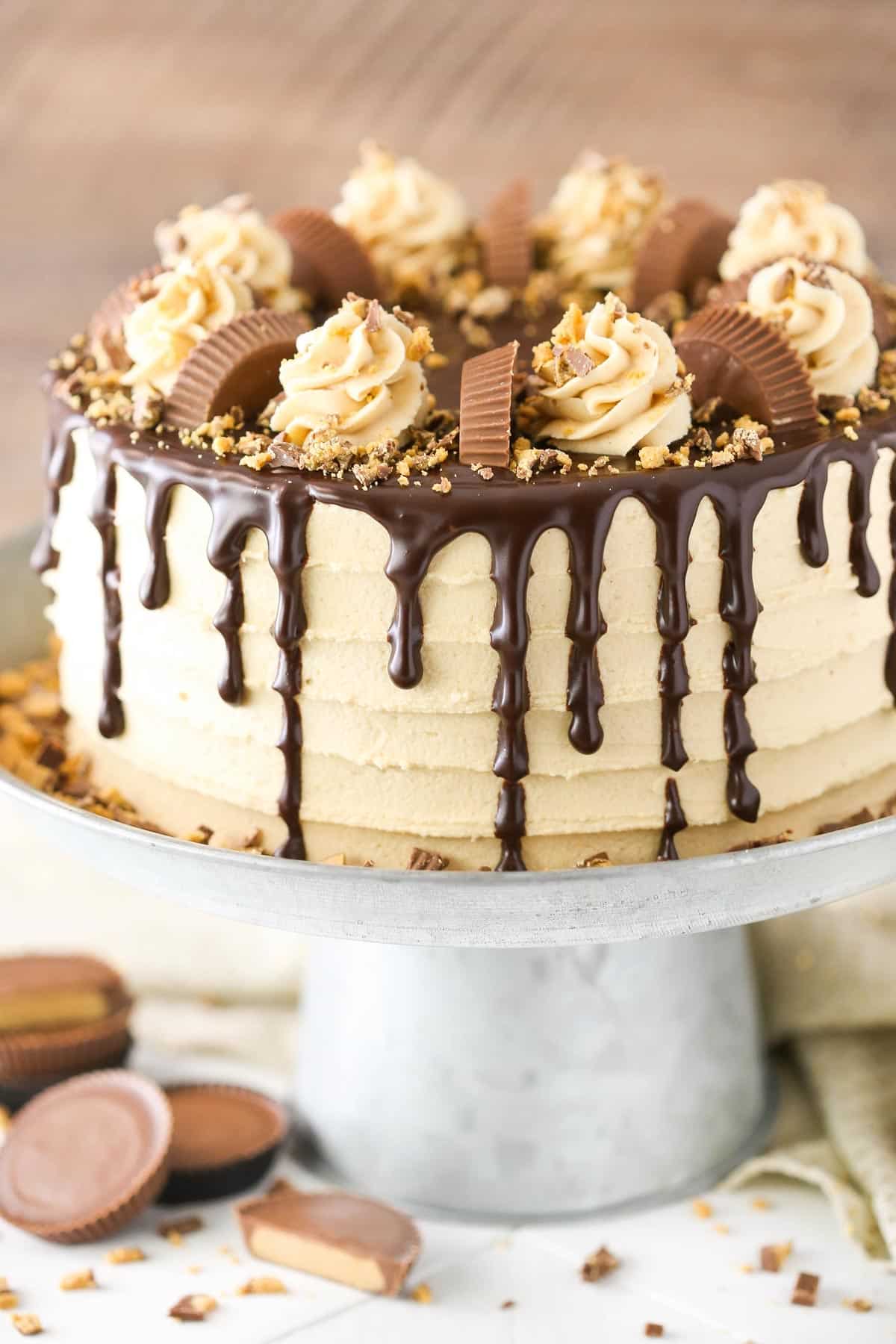 This peanut butter chocolate cake is made with layers of moist chocolate cake, peanut butter frosting and chopped Reese’s peanut butter cups. Close up of a peanut butter chocolate layer cake on a silver cake stand.