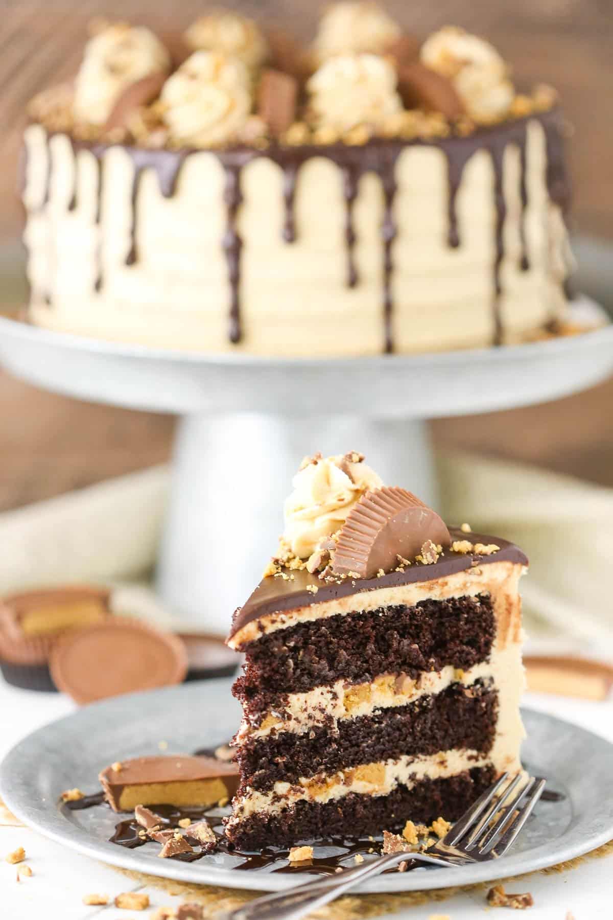 A slice of peanut butter chocolate layer cake on a silver plate with the rest of the cake in the background.