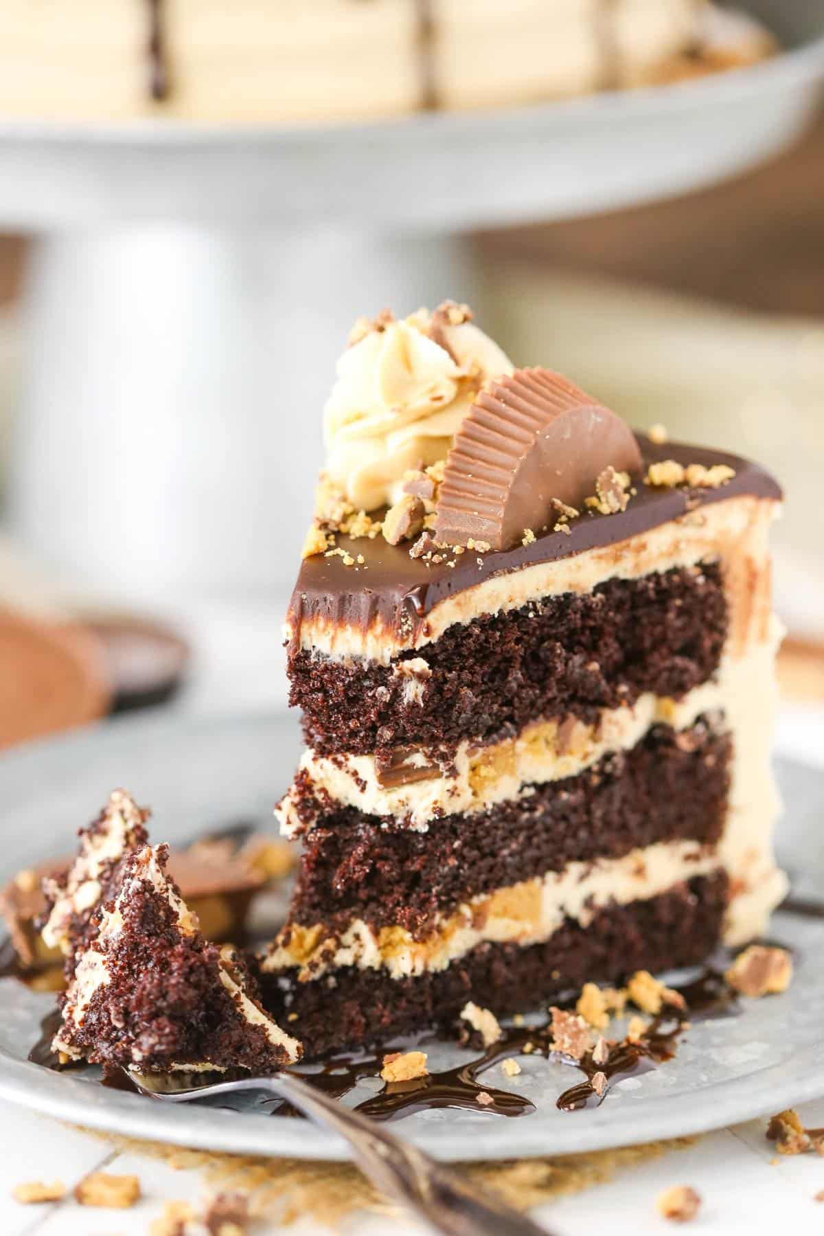 This peanut butter chocolate cake is made with layers of moist chocolate cake, peanut butter frosting and chopped Reese’s peanut butter cups. A slice of peanut butter chocolate layer cake with a bite removed on a silver plate.