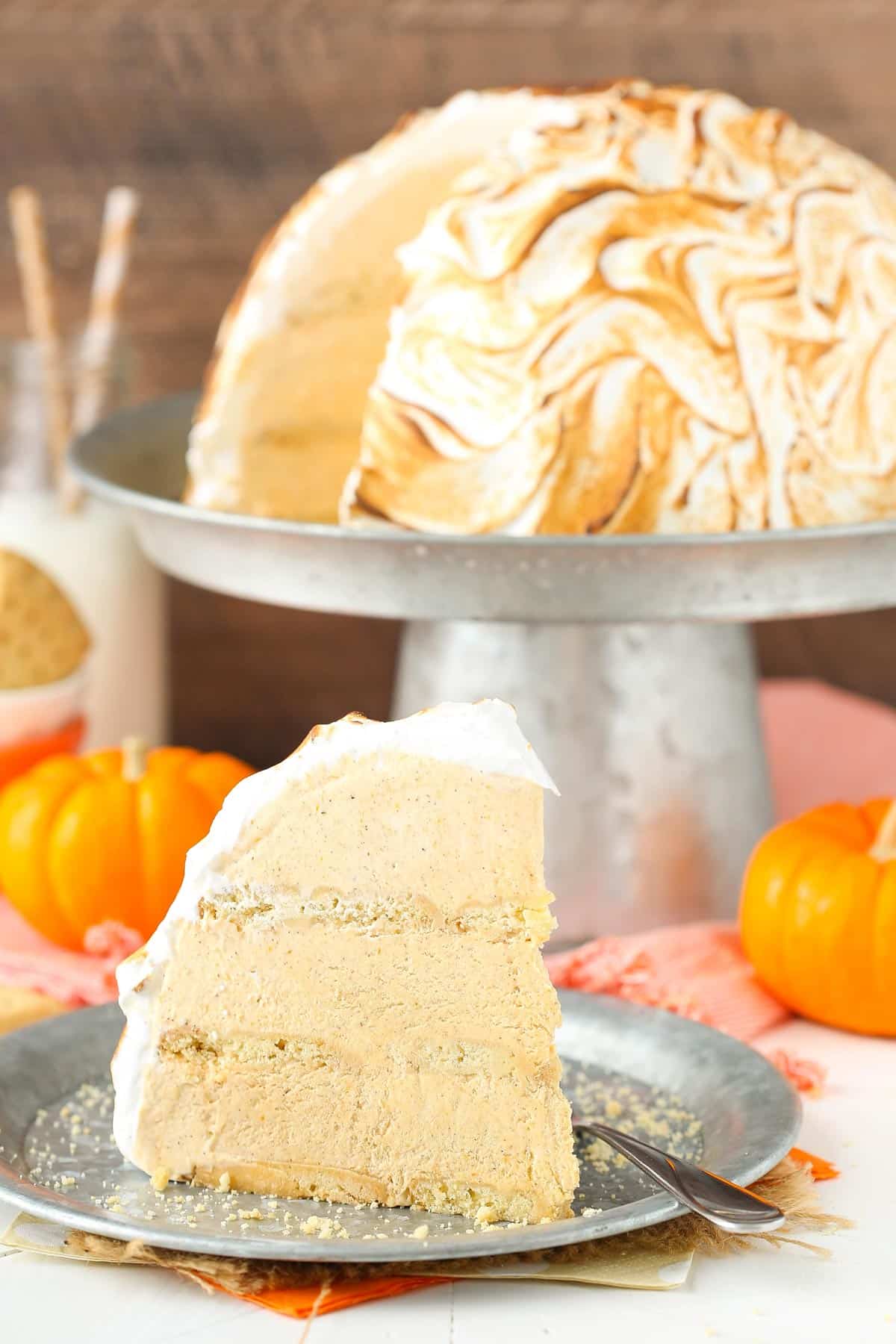 A slice of pumpkin spice baked Alaska on an orange plate with the rest of the cake in the background.