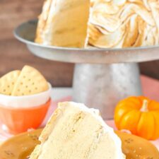 A slice of pumpkin spice baked Alaska on an orange plate with the rest of the cake in the background.