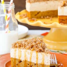 A slice of caramel pumpkin spice blondie streusel cheesecake on an orange plate with the rest of the cake in the background.