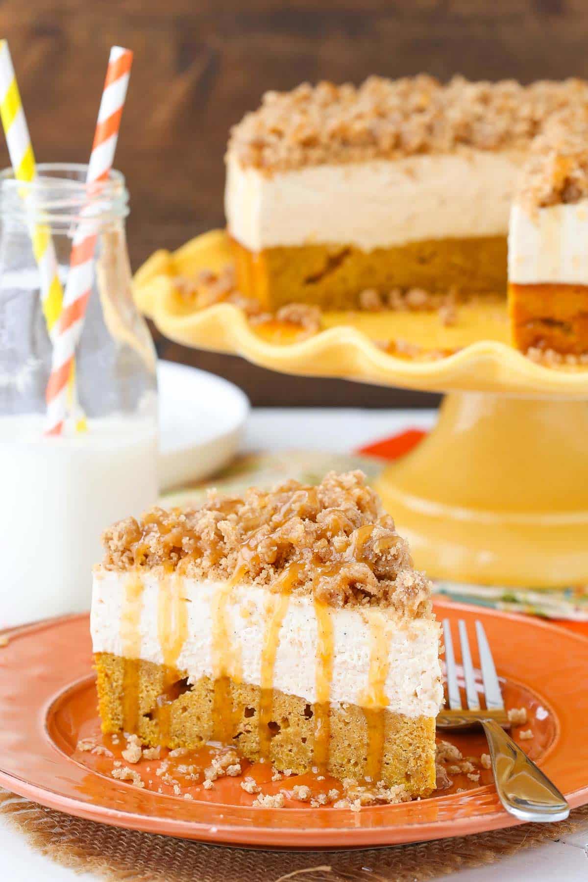 A slice of caramel pumpkin spice blondie streusel cheesecake on an orange plate with the rest of the cake in the background.
