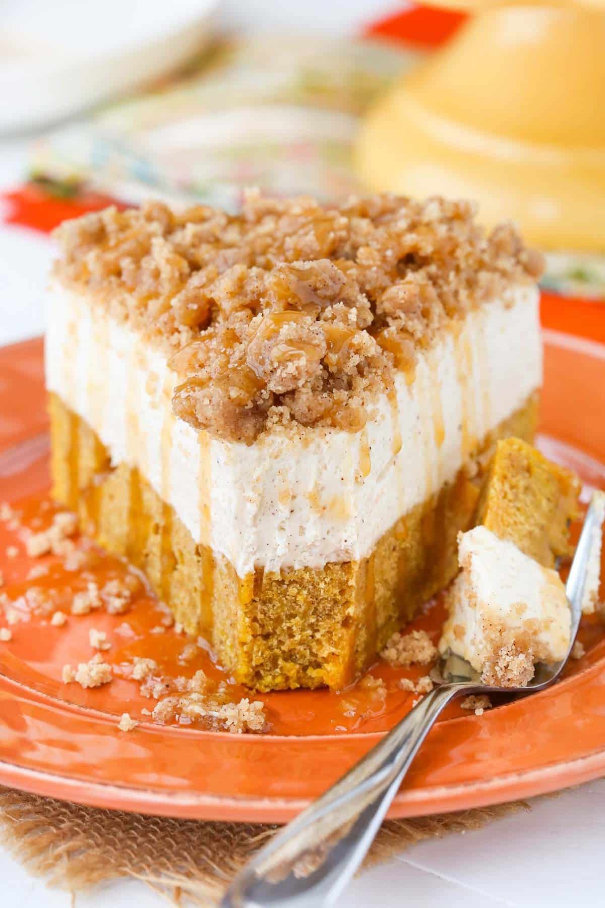 A slice of caramel pumpkin spice blondie streusel cheesecake on an orange plate with a bite removed on a fork.