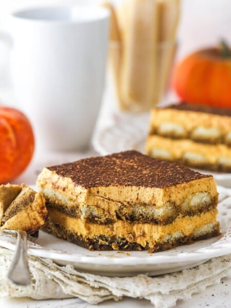 A slice of pumpkin tiramisu on a plate with a bite taken out of it.