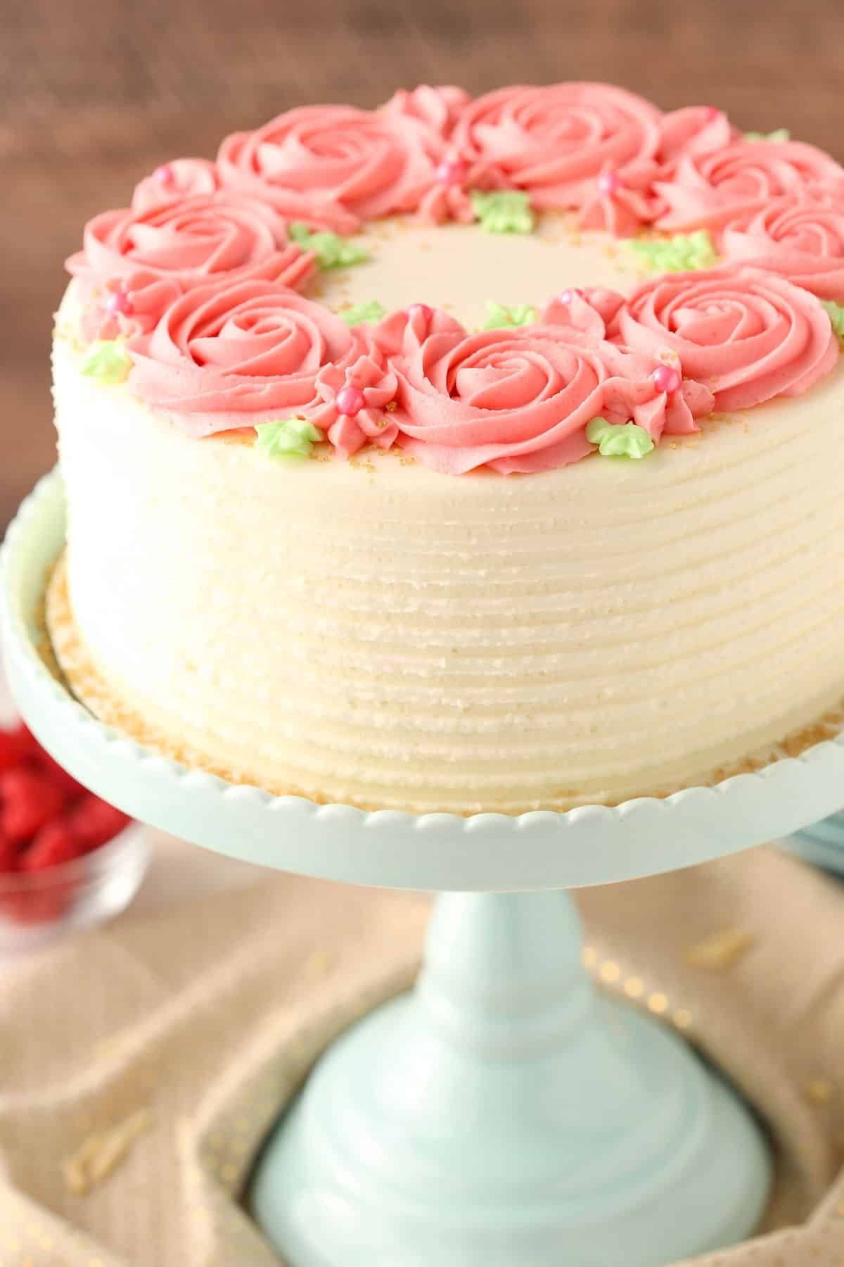 Close up of a raspberry almond layer cake on a teal cake stand.