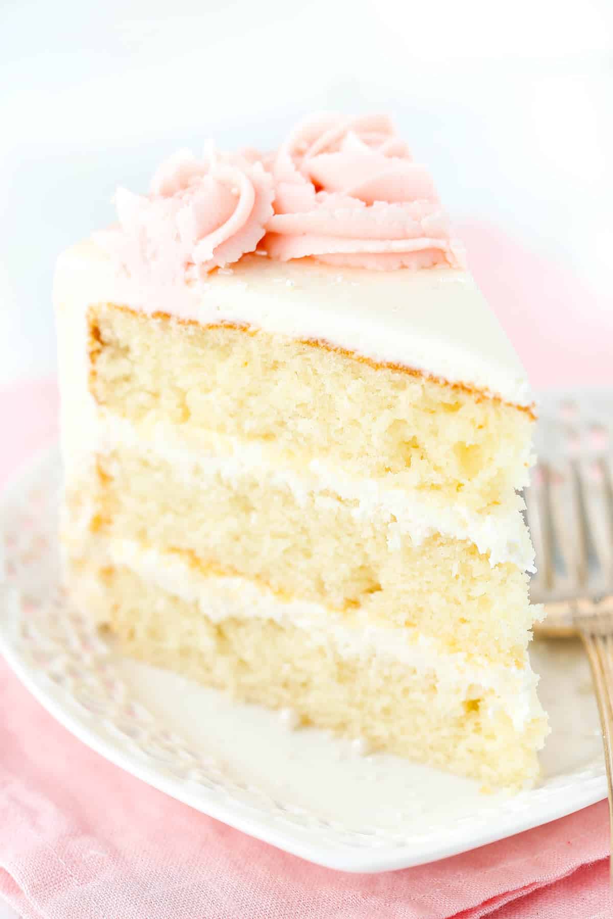 A slice of rose water vanilla layer cake on a white plate.