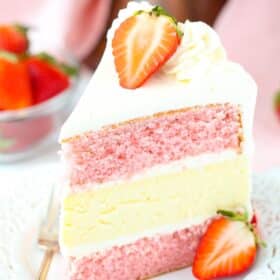 A slice of strawberries and cream cheesecake cake on a small white plate.