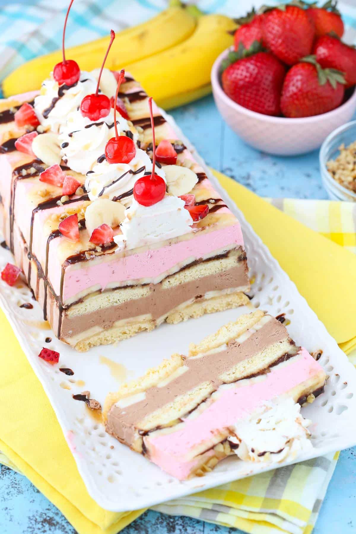 A banana split ice cream cake loaf on a white tray with one slice removed.