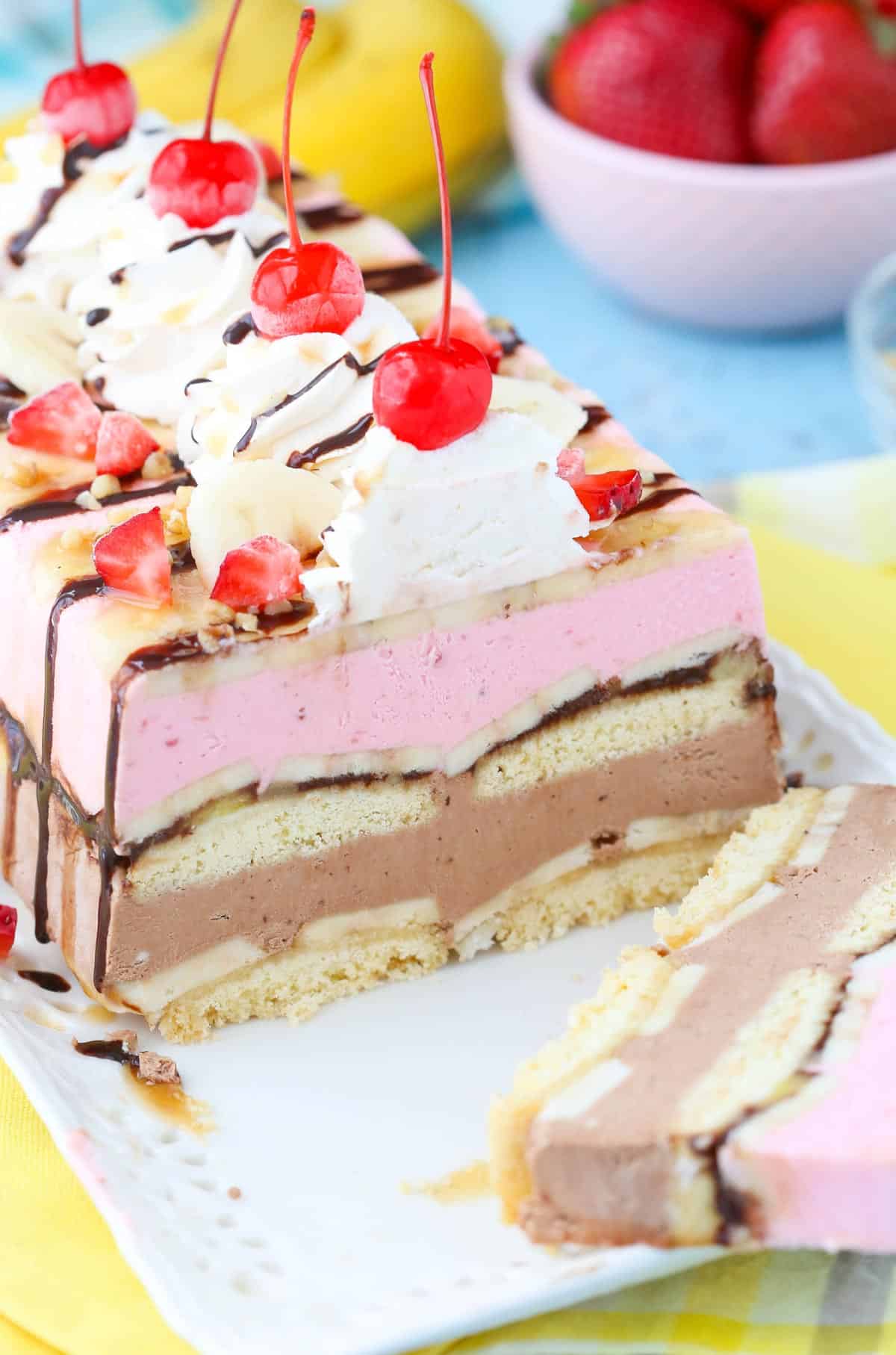 Close up of a banana split ice cream cake loaf with a slice removed on a white tray.