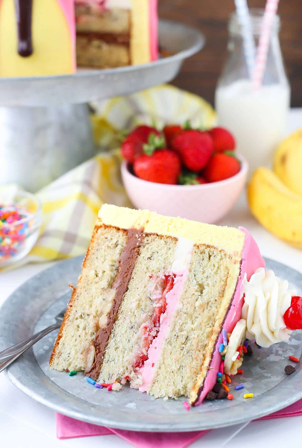 A slice of banana split layer cake on a small silver plate.