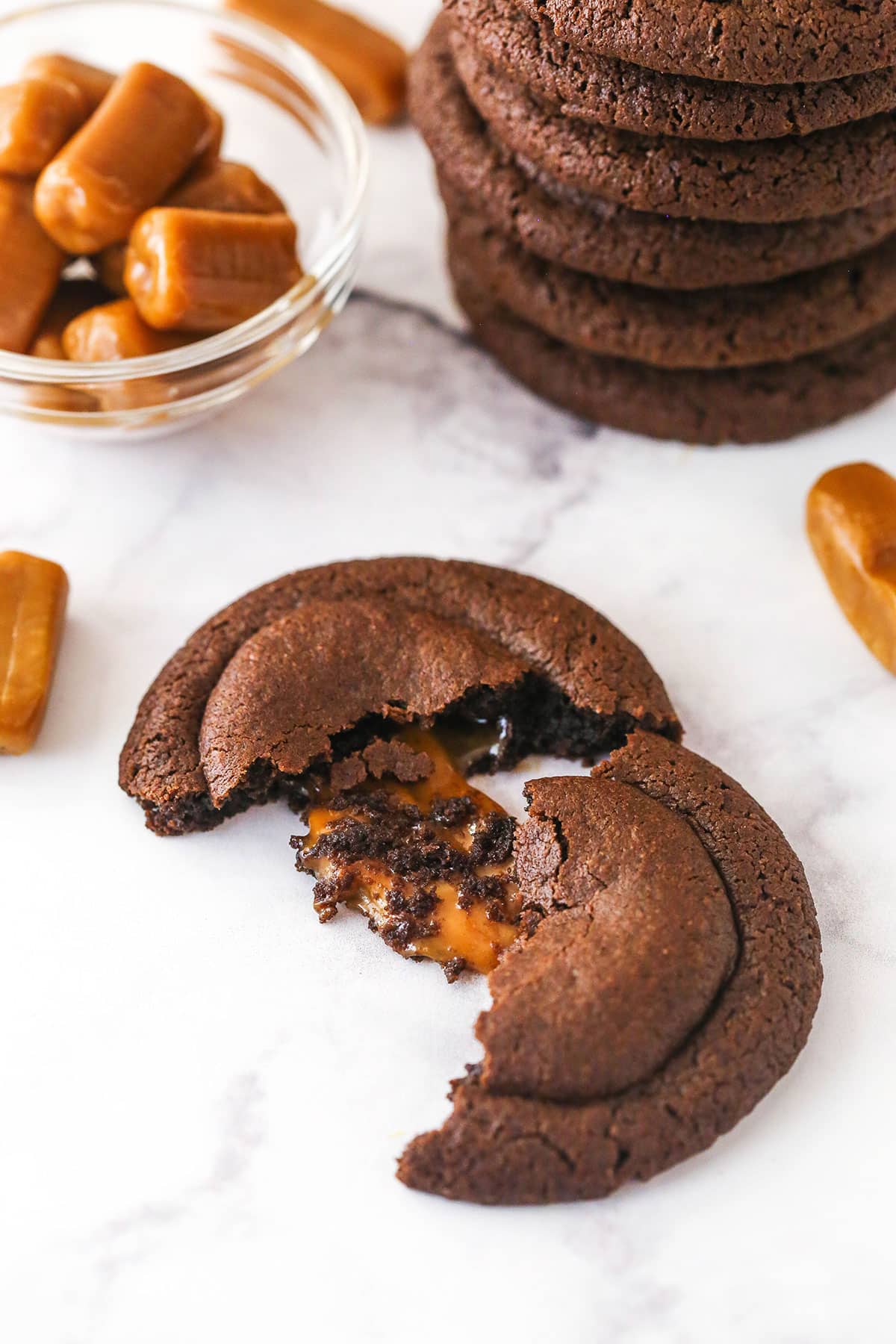 These caramel stuffed cookies feature a soft, chewy chocolate cookie dough that perfectly complements a gooey, sweet caramel center. A caramel stuffed cookie broken in half to reveal the gooey caramel filling.