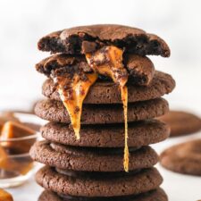 A stack of caramel stuffed cookies. The top one is broken in half to reveal the gooey caramel filling.
