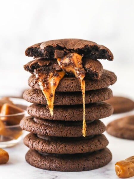 A stack of caramel stuffed cookies. The top one is broken in half to reveal the gooey caramel filling.