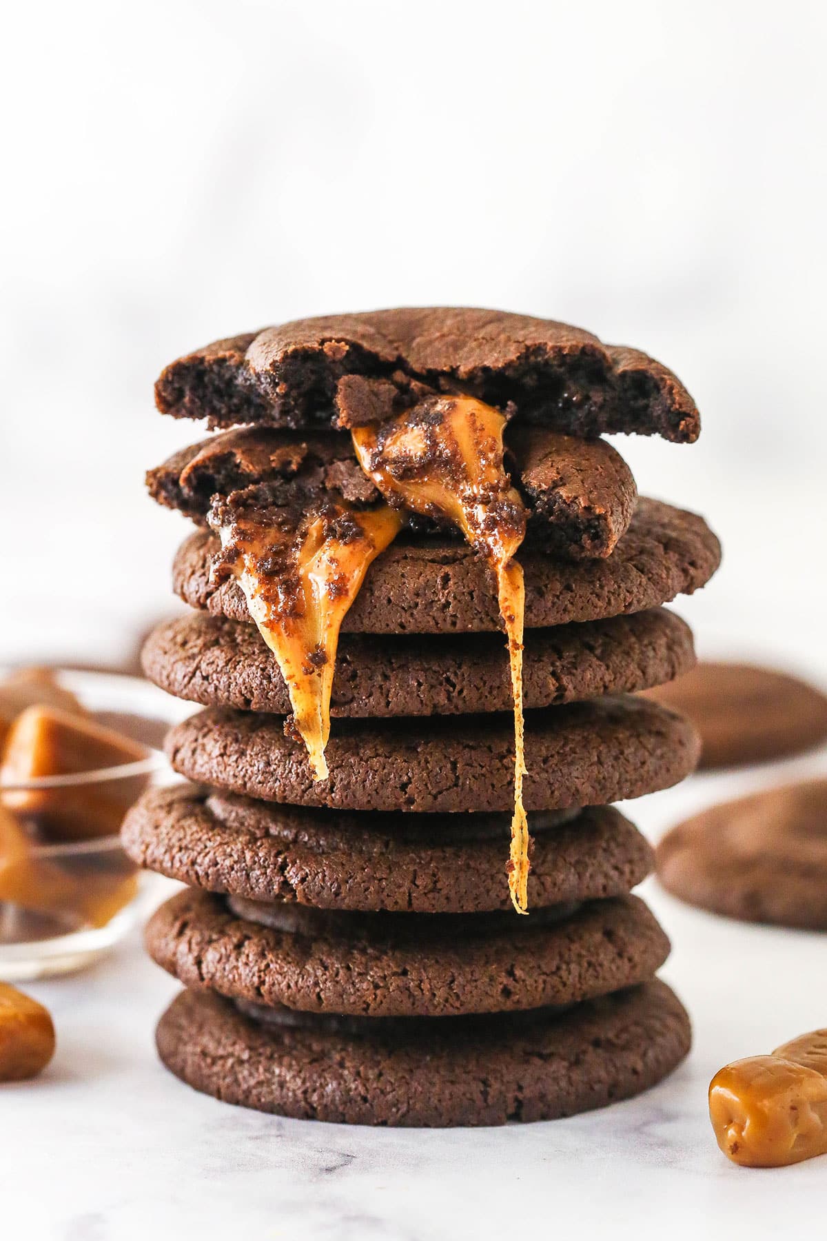 A stack of caramel stuffed cookies. The top one is broken in half to reveal the gooey caramel filling.