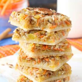 Six carrot cake shortbread bars stacked one on top of the other with a bite taken out of the top bar.