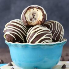 Side view of a light blue bowl filled with chocolate chip cookie dough cheesecake balls with a bite taken out of top cookie dough ball.