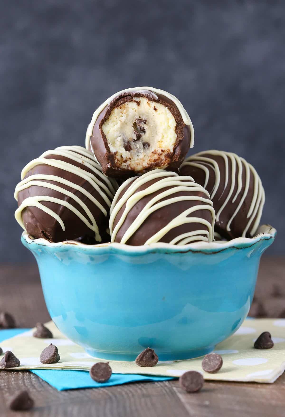 Side view of a light blue bowl filled with chocolate chip cookie dough cheesecake balls with a bite taken out of top cookie dough ball.