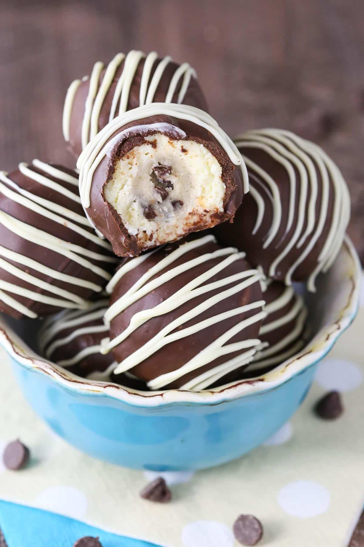 A light blue bowl filled with chocolate chip cookie dough cheesecake balls with a bite taken out of top cookie dough ball.