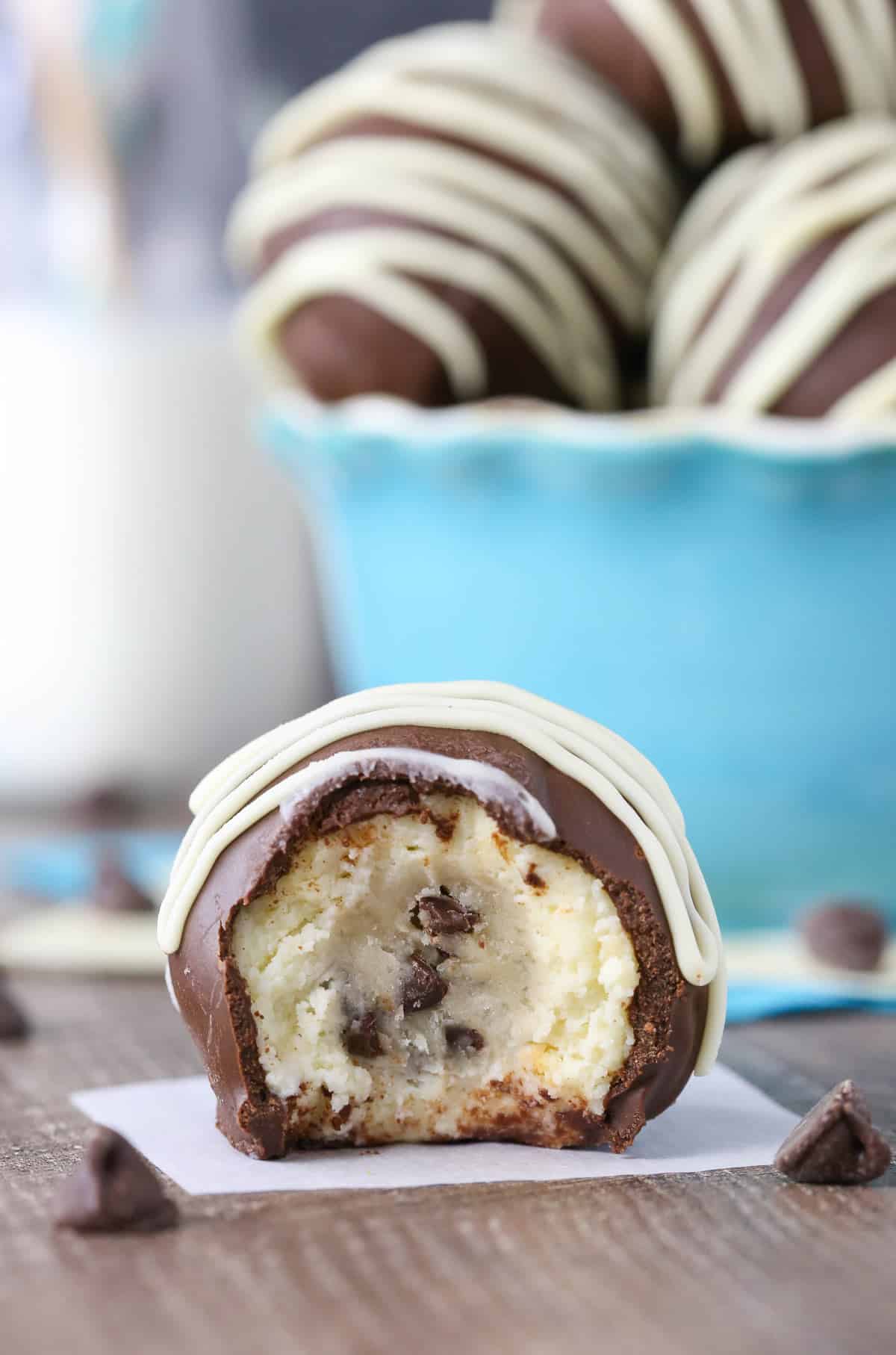 A chocolate chip cookie dough cheesecake ball with a bite out of it on a piece of parchment.