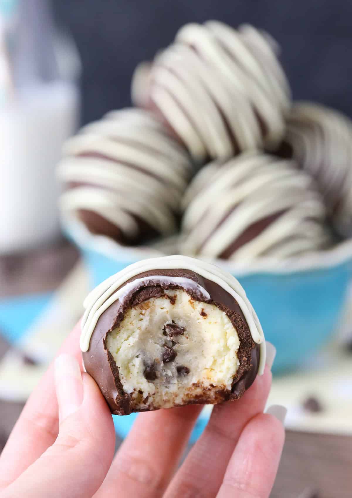 Hand holding up a chocolate chip cookie dough cheesecake ball with a bite removed to show center.