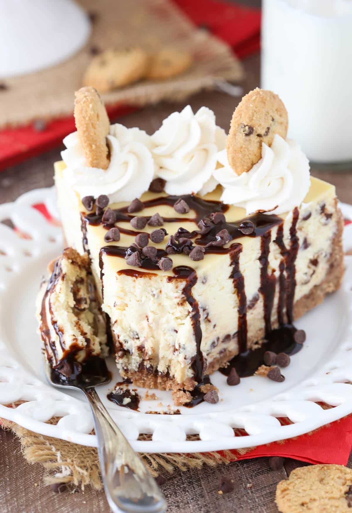 A slice of chocolate chip shortbread cheesecake drizzled with chocolate with a bite removed on a fork.