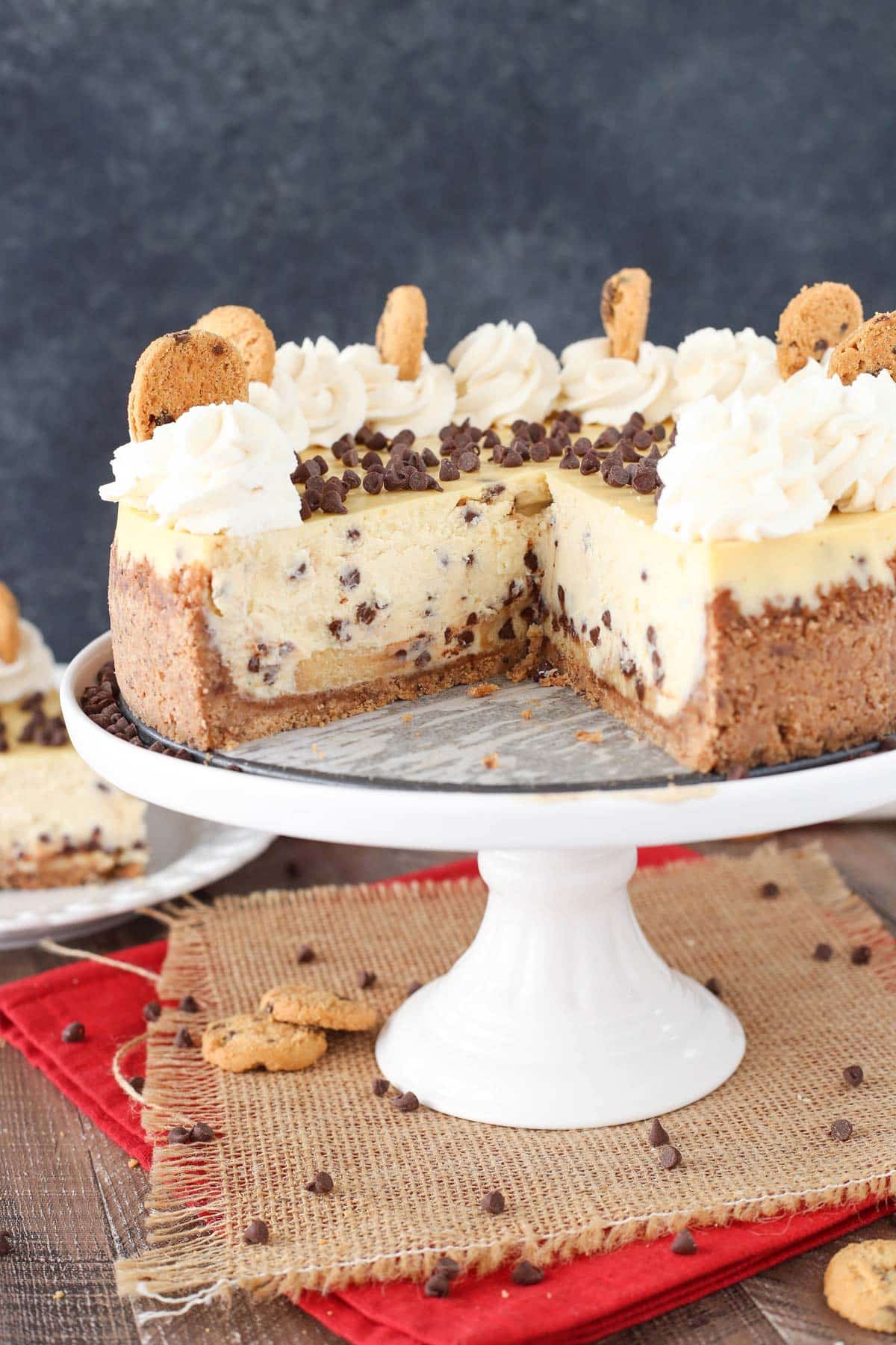 A chocolate chip shortbread cheesecake on a white cake stand with a large slice removed to show inside layers.