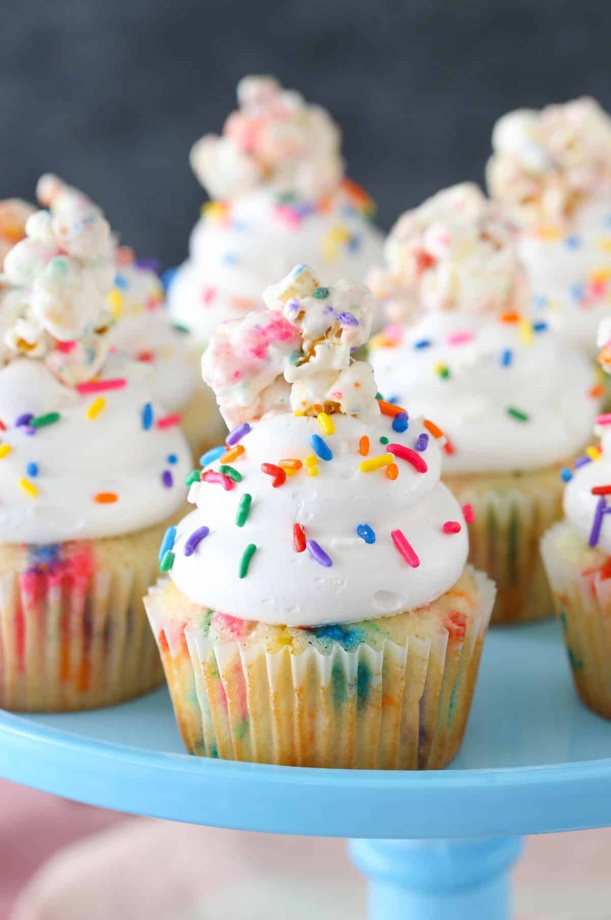 Close up of a funfetti popcorn marshmallow treat cupcake on a light blue cake stand.
