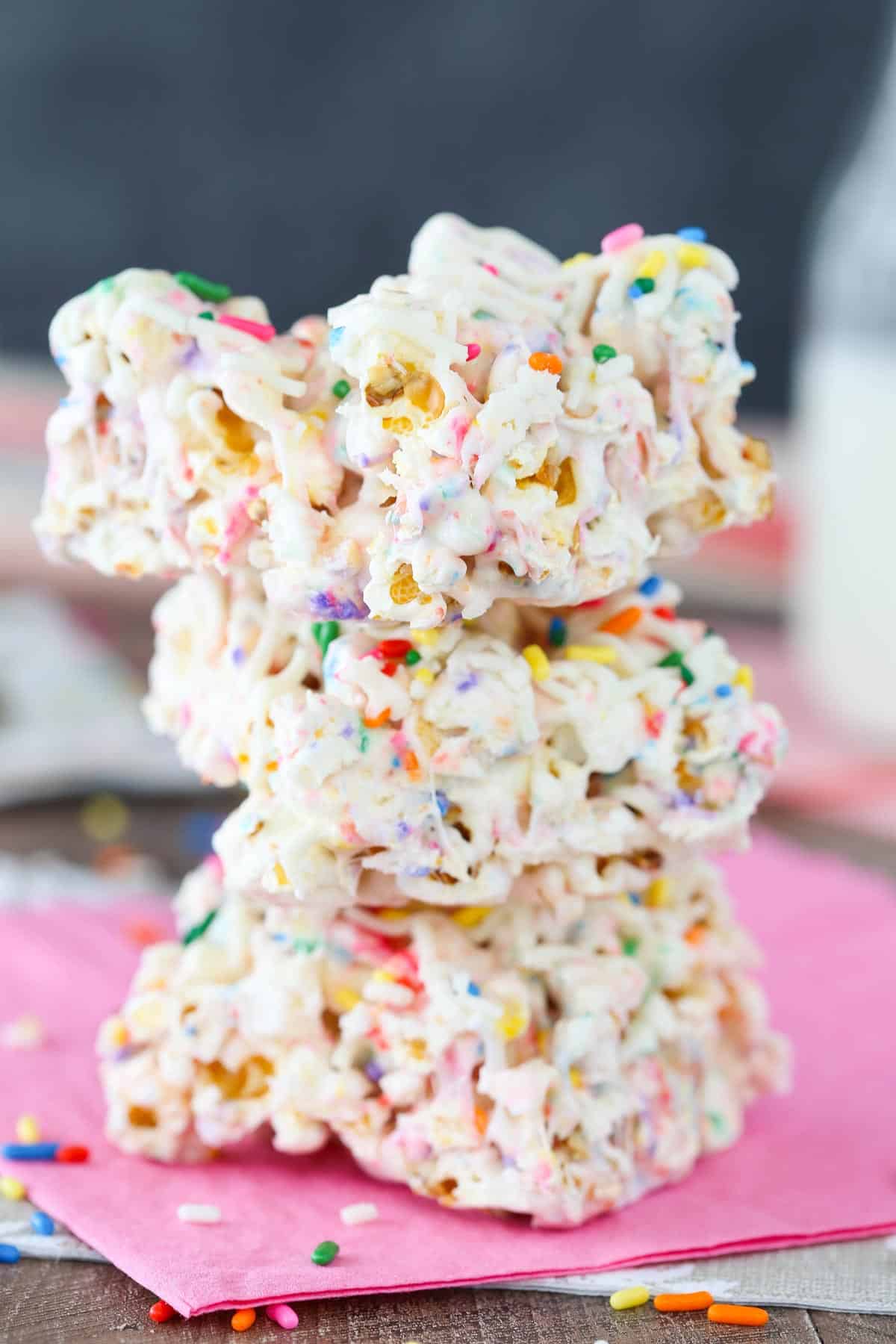 A stack of three funfetti marshmallow popcorn treats on a light pink napkin.