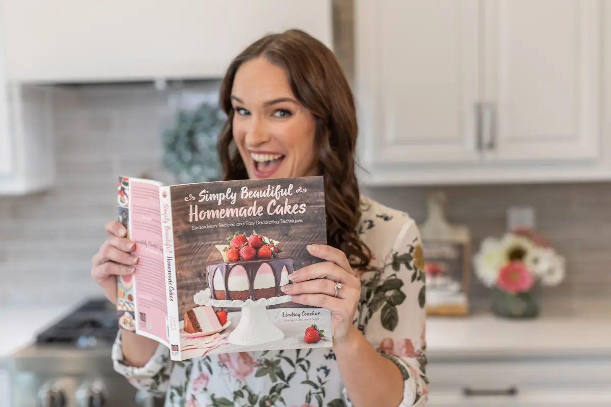 Lindsay, author of Life Love and Sugar, smiling and holding her cookbook.