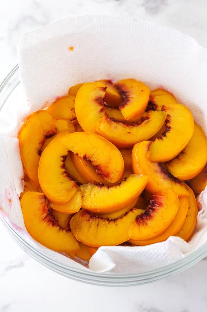 Peach slices in a paper towel-lined bowl.