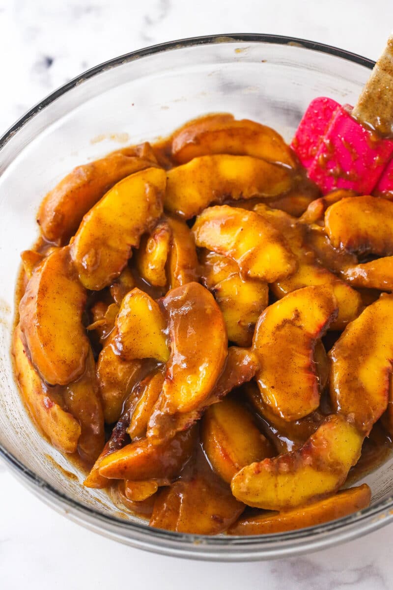 Tossing peach slices with sugars, flour, salt, and cinnamon.
