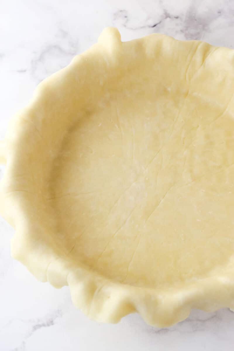 Pie dough fit into a pie pan with a little dough hanging over the edges.