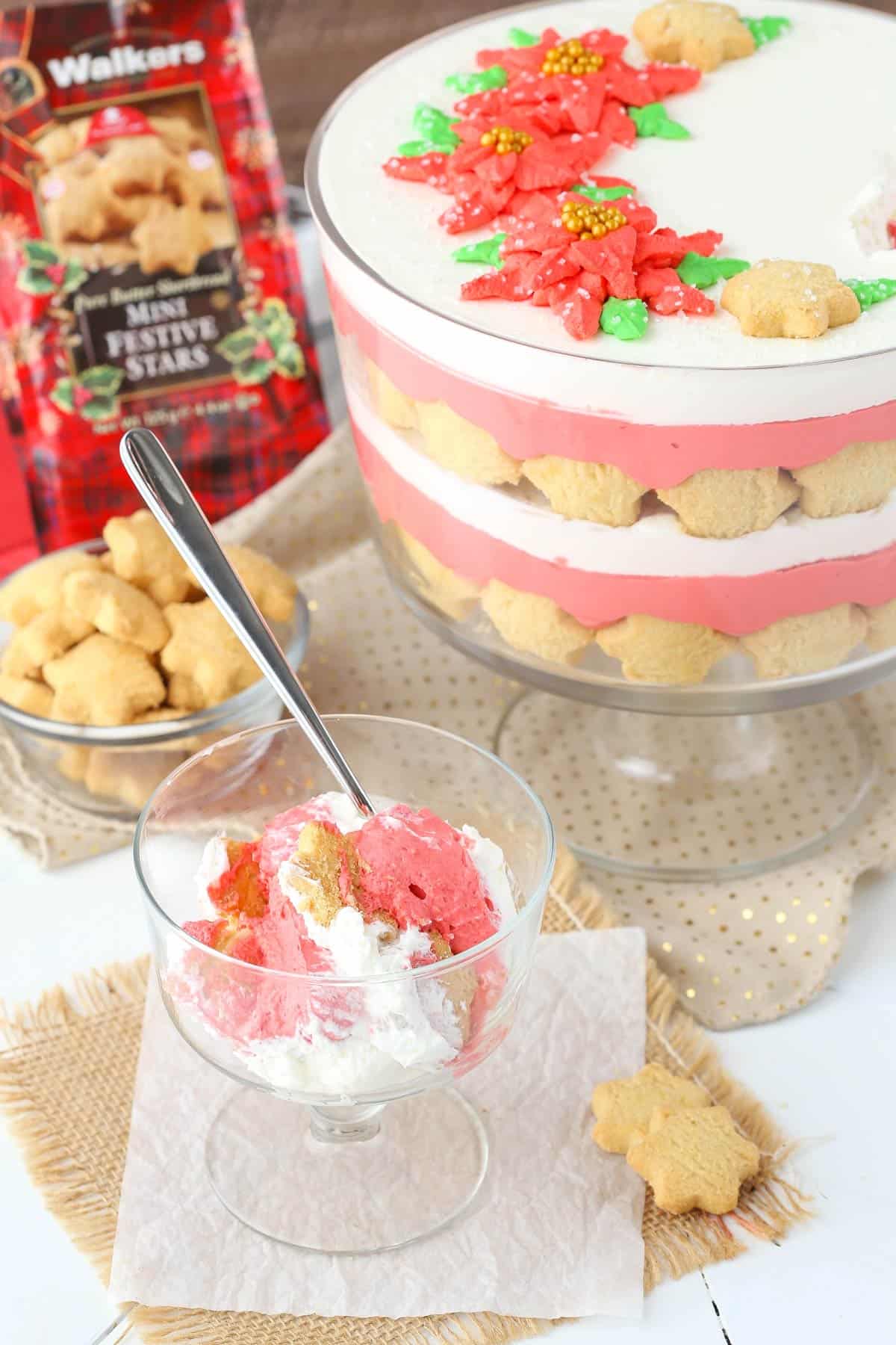 A serving of red velvet shortbread trifle in a footed dessert cup with the rest of the trifle in the background.