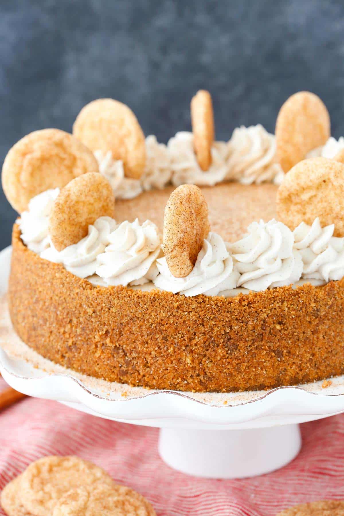 This snickerdoodle cheesecake's got a chewy cinnamon sugar crust and a creamy dulce de leche filling, topped with white chocolate ganache. A snickerdoodle dulce de leche cheesecake on a ruffled cake stand.