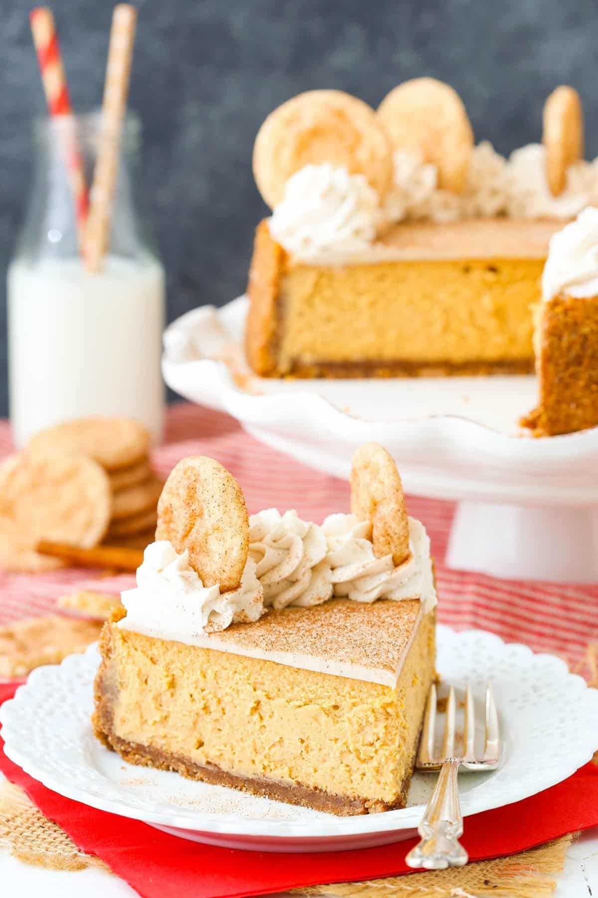 A slice of snickerdoodle dulce de leche cheesecake on a small white plate with the rest of the cheesecake in the background.