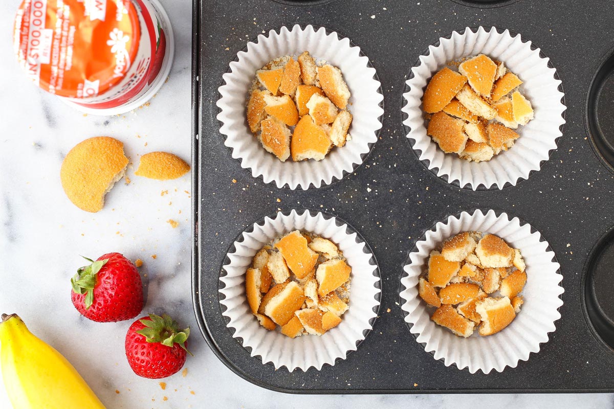 Top view of a cupcake pan with crushed vanilla wafer cookies in the bottom of four lined cups.