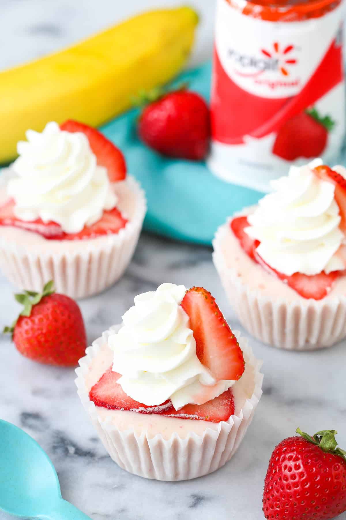 Three strawberry banana frozen yogurt cupcakes with yogurt in the background.