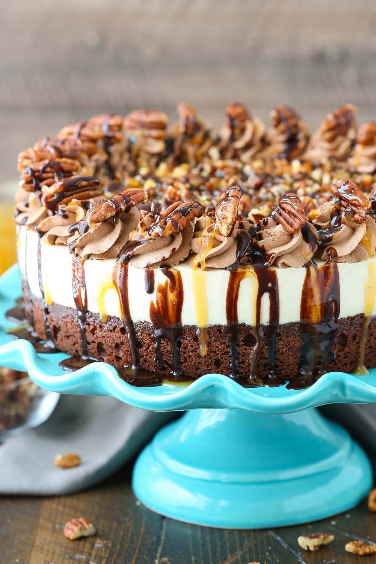 Side view of a turtle brownie cheesecake on a blue cake stand.