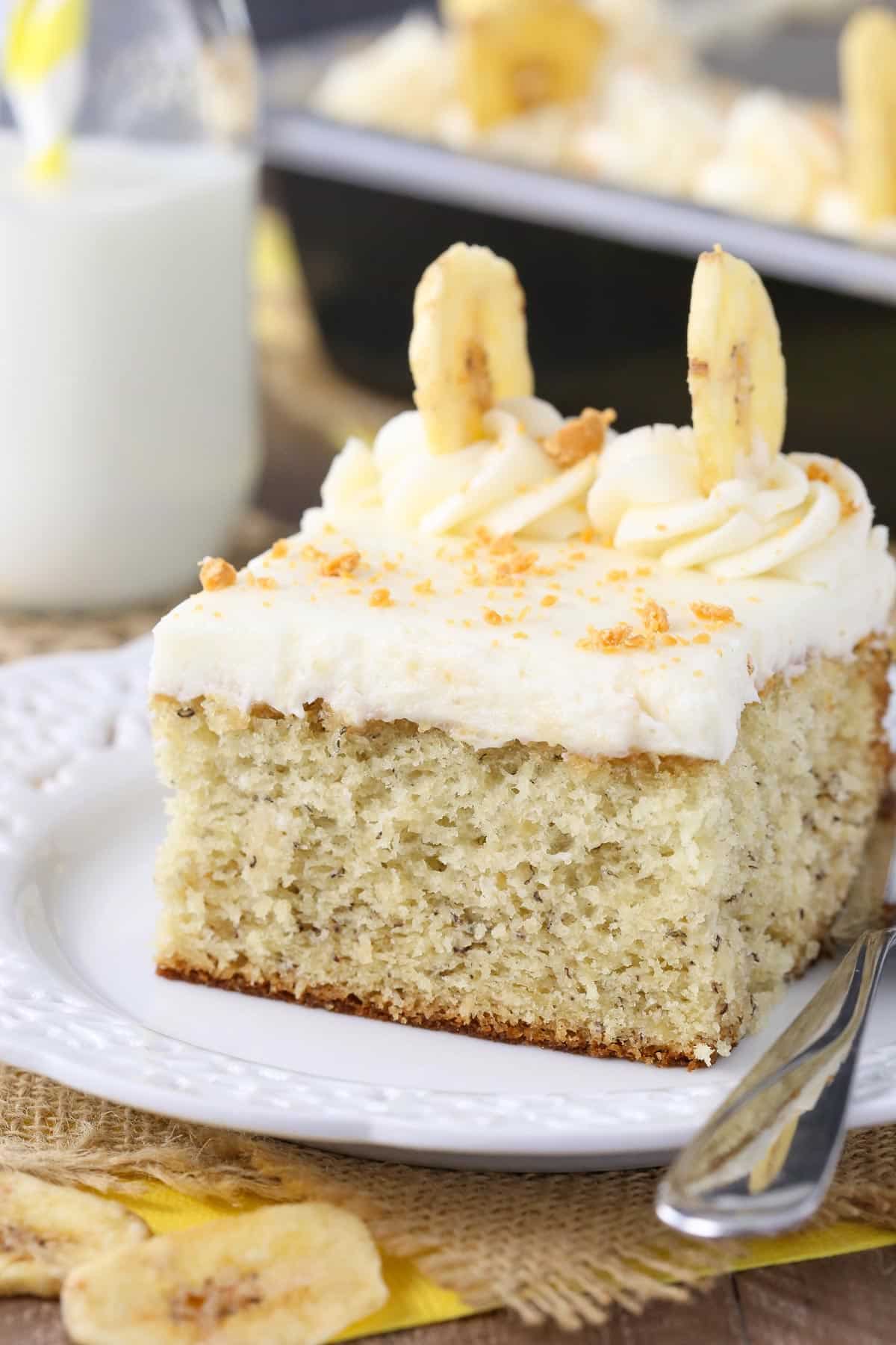 Close up of a slice of banana cake with cream cheese frosting on a white plate.