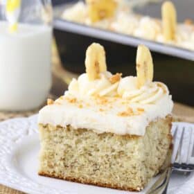 A slice of banana cake with cream cheese frosting on a small white plate.