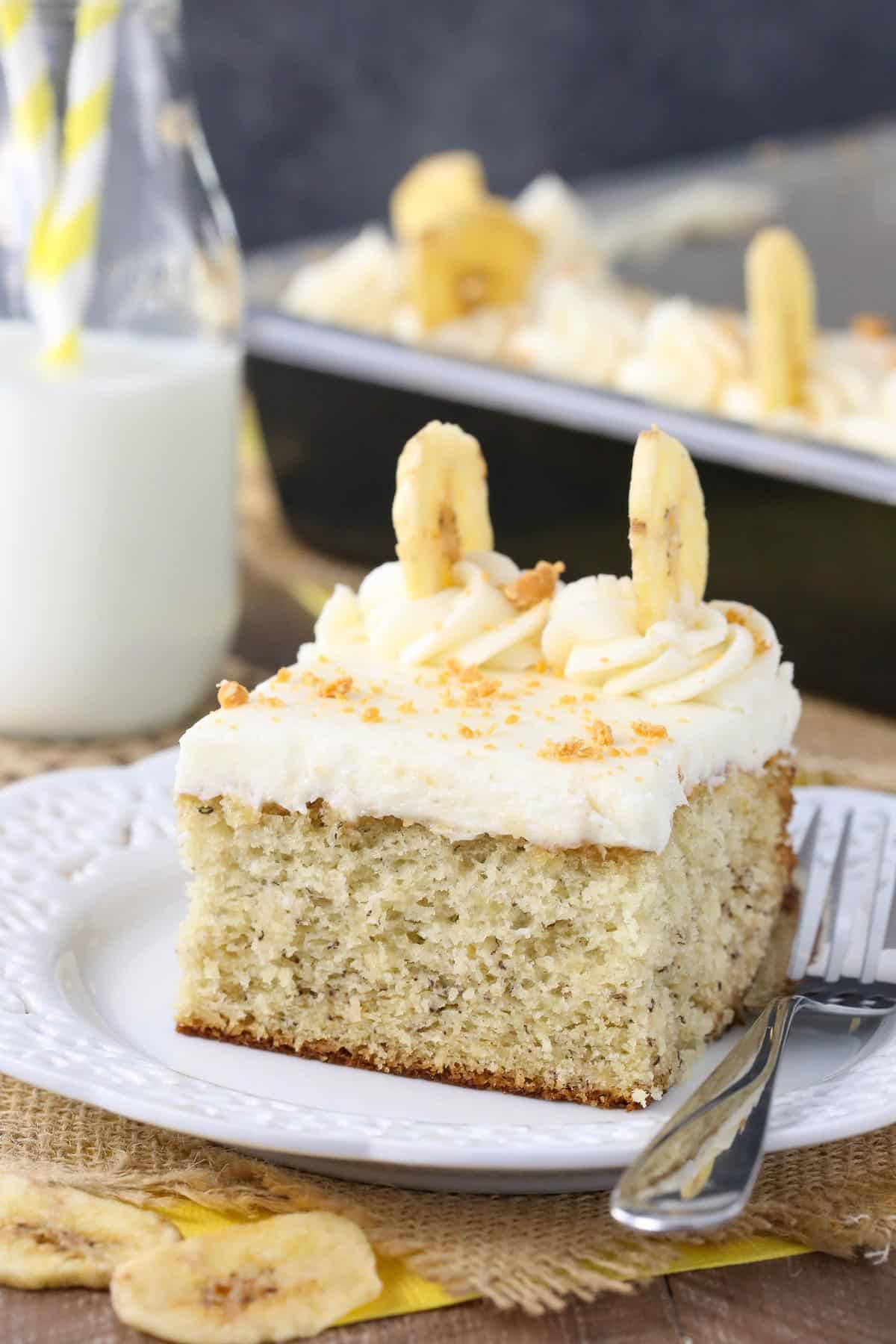 A slice of banana cake with cream cheese frosting on a small white plate.