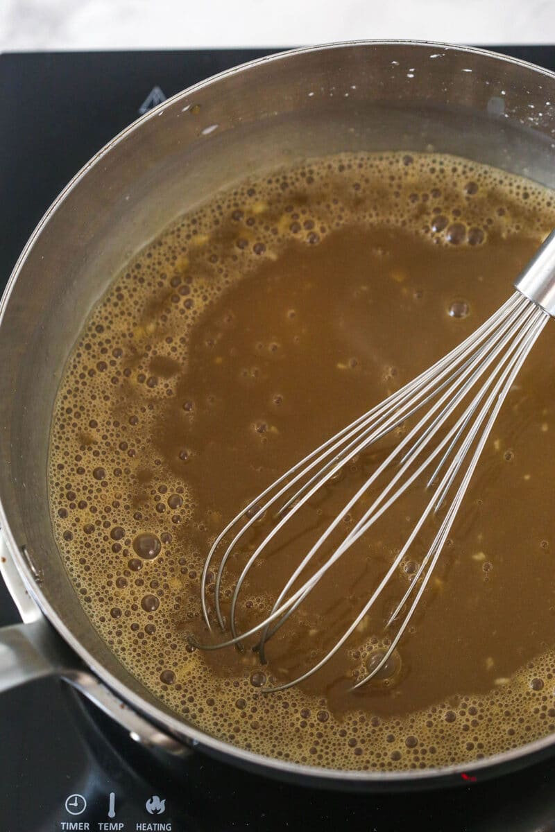 Whisking dak brown sugar dissolved in water into a mixture of warm cornstarch, salt, milk, and heavy cream in a saucepan.
