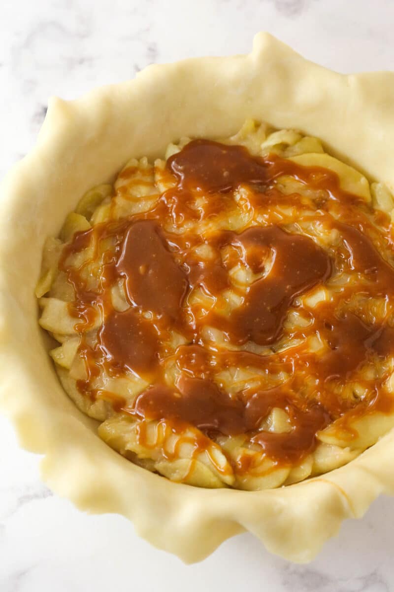 Layering caramel sauce over apple filling in a pie crust.