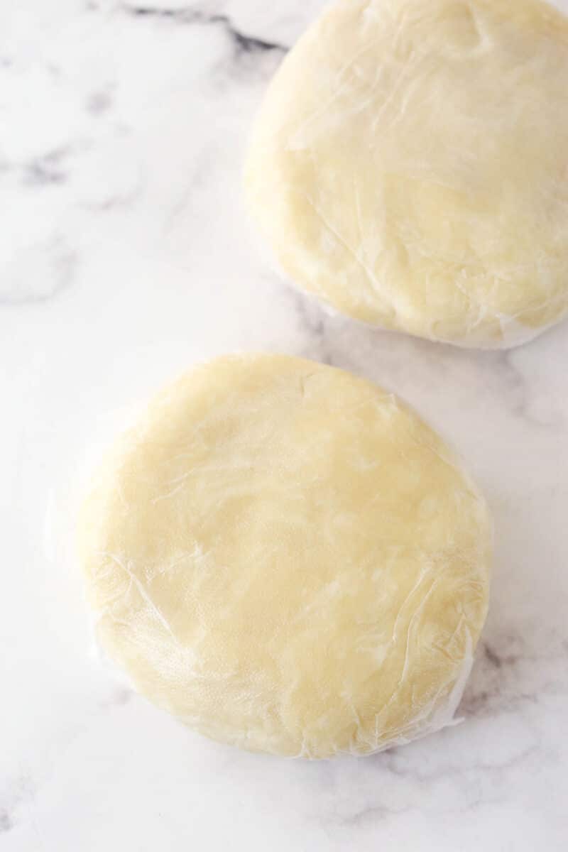 Pie dough formed into disks and wrapped in plastic wrap.
