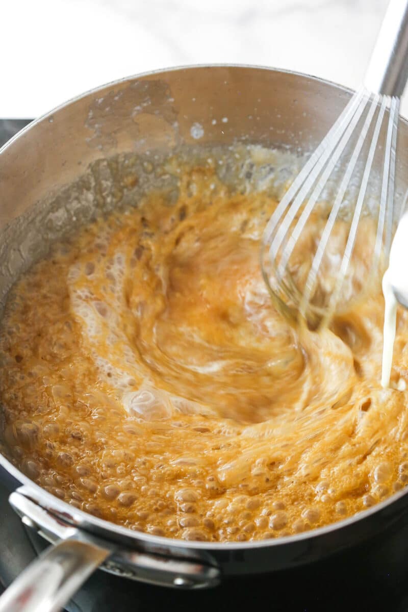 Whisking heavy cream into caramelized butter and sugar.