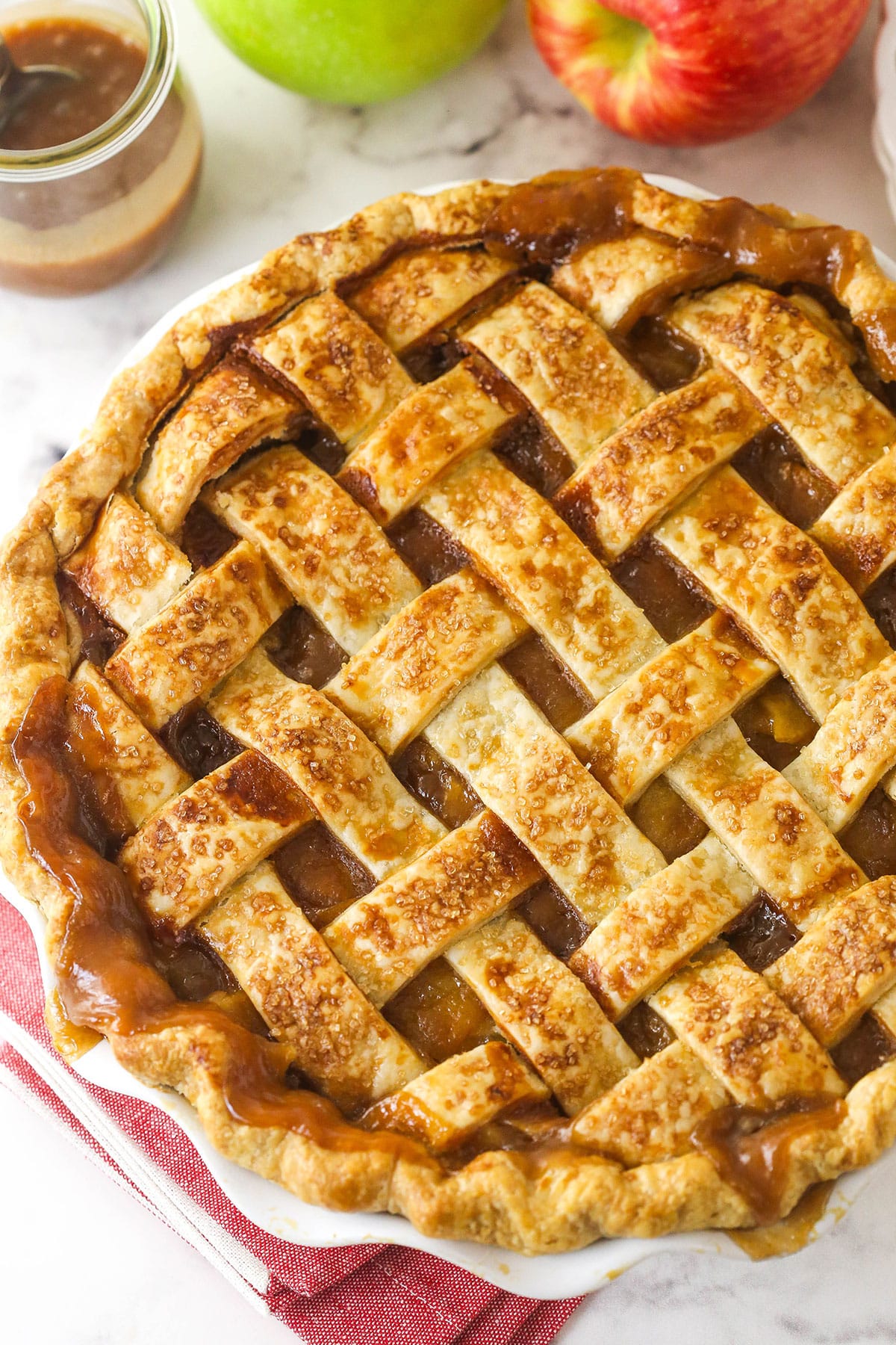 This caramel apple pie recipe takes a classic dessert to the next level with a gooey caramel sauce folded into the filling. Overhead image of caramel apple pie in a pie pan.