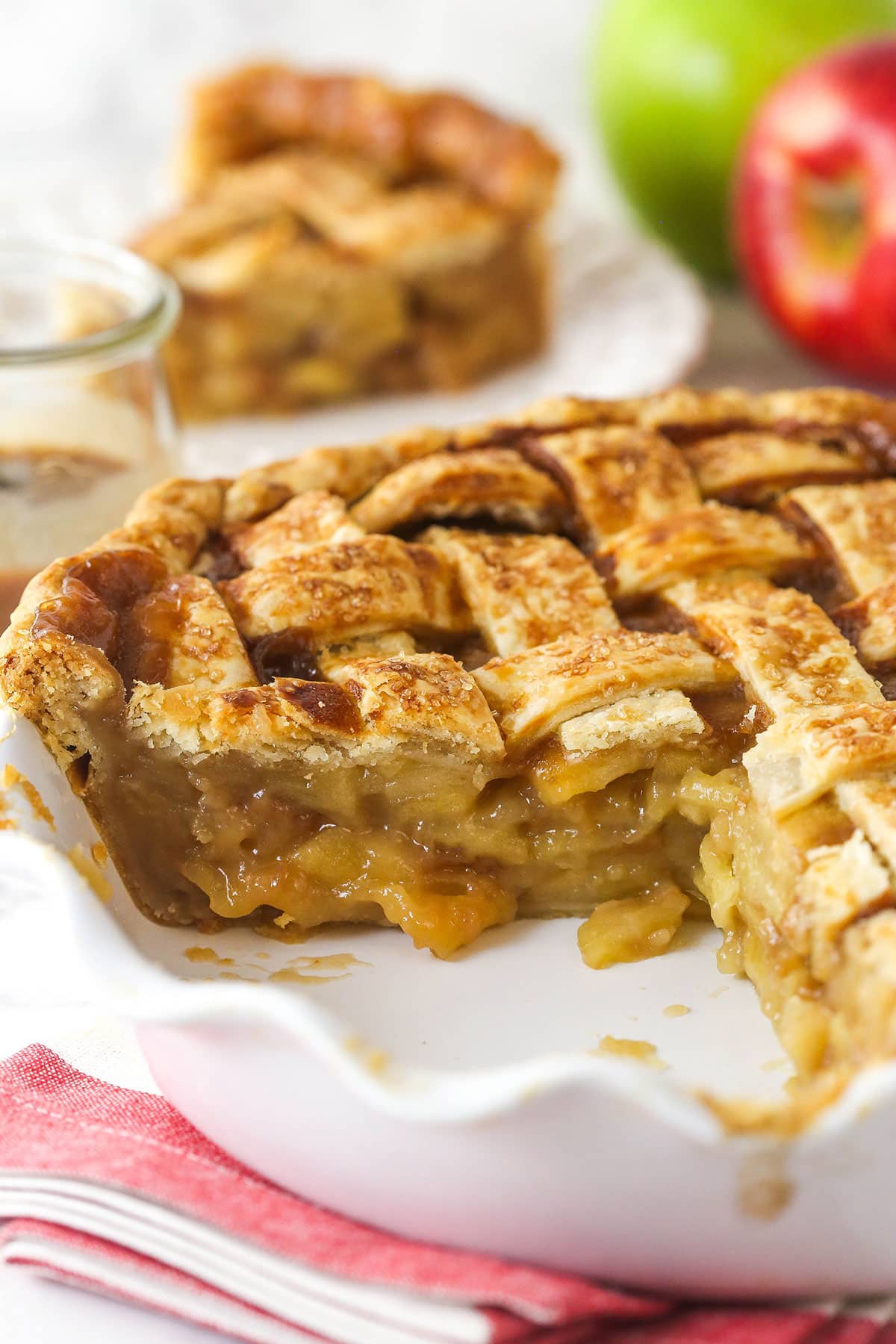 This caramel apple pie recipe takes a classic dessert to the next level with a gooey caramel sauce folded into the filling. Caramel apple pie in a pie pan with a couple of slices removed.