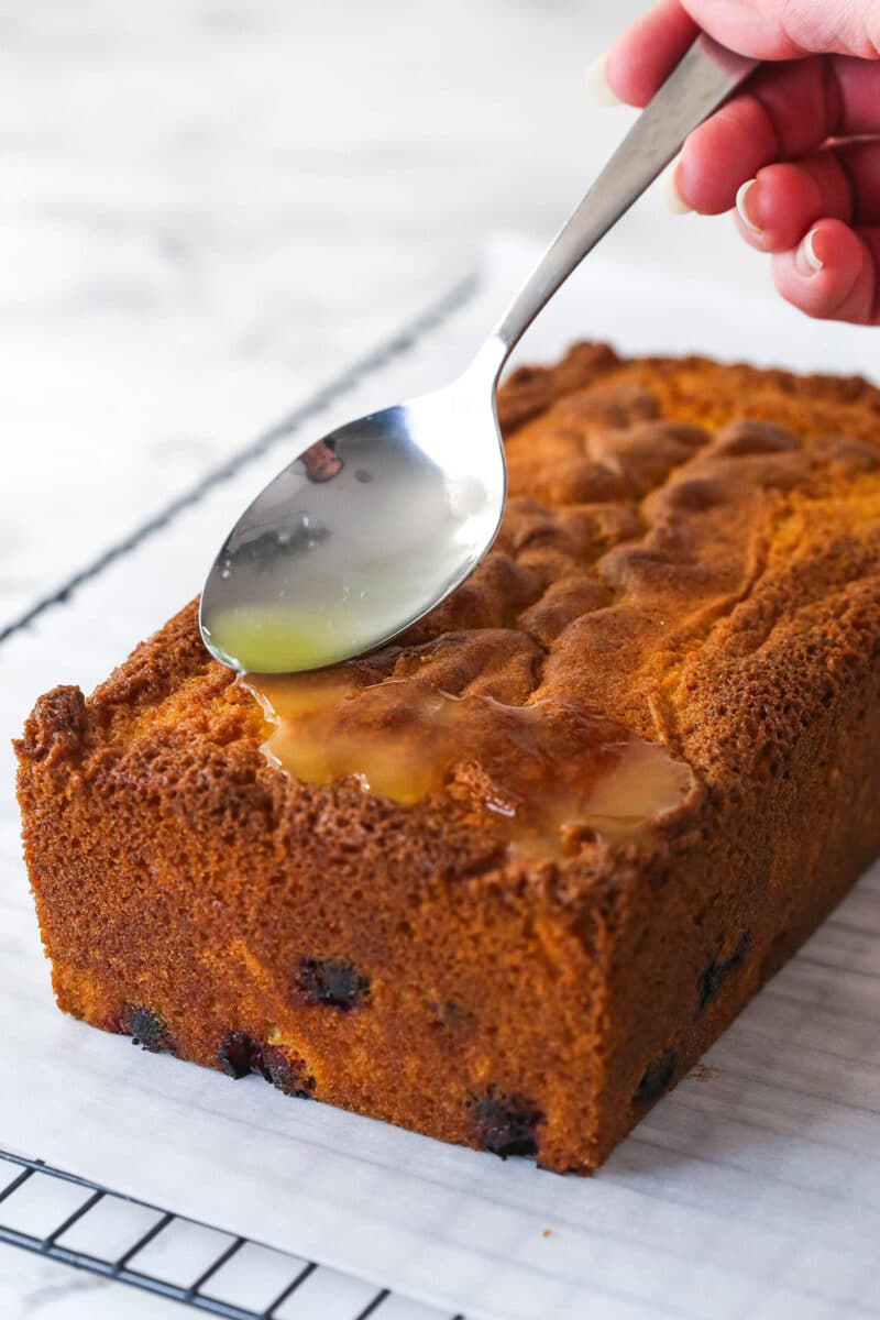 Spooning orange syrup over orange cranberry loaf cake.