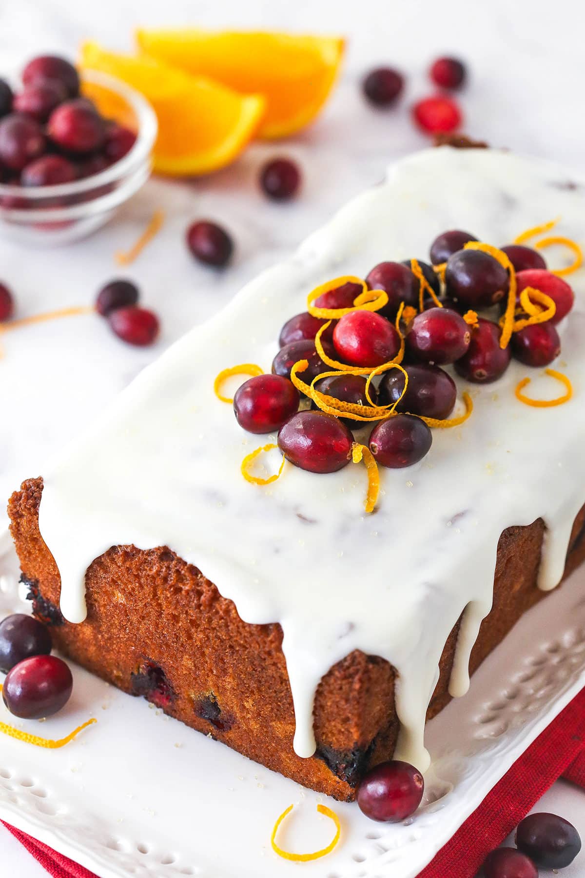 This glazed cranberry orange loaf combines bright, tangy flavors with a perfectly moist, tender crumb. It's the perfect holiday treat! An orange cranberry loaf on a serving tray.